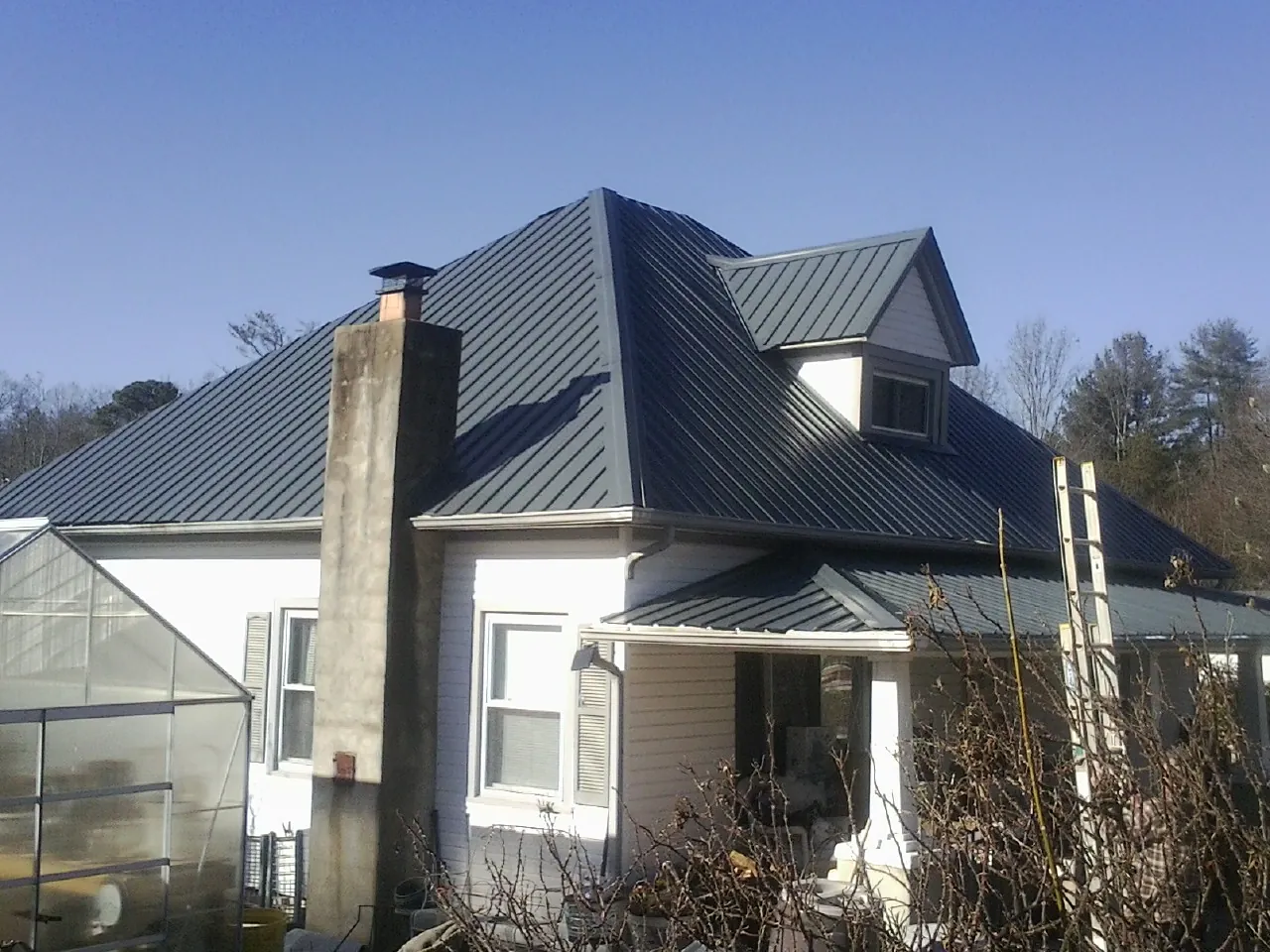 Dark blue standing seam metal roof on a white farmhouse with dormer — Slate & Tile Roof Repair by Roofing Brothers in Molino