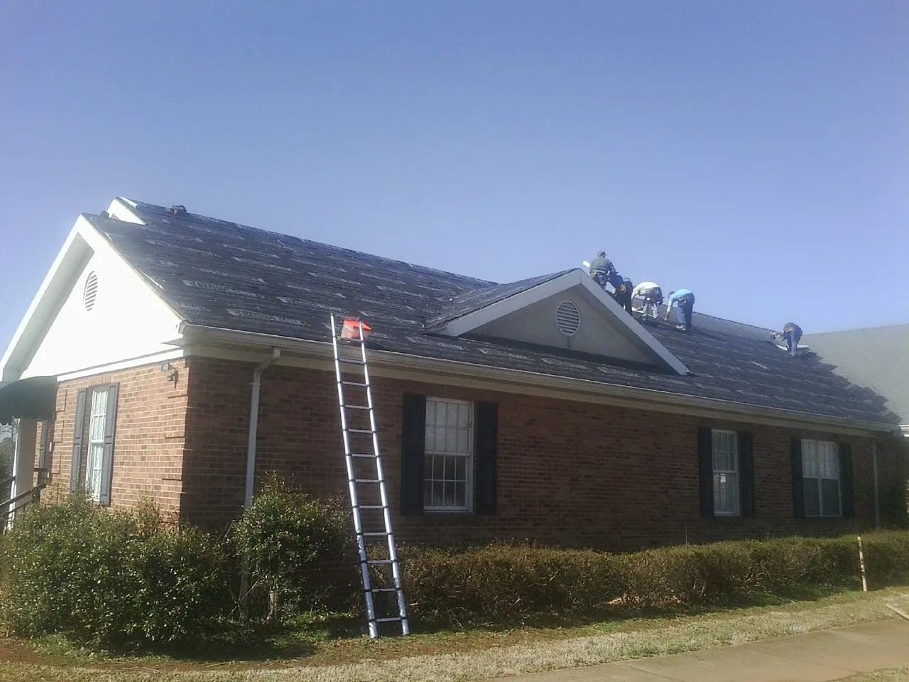 Crew tearing shingles off a brick ranch roof with a ladder set — Emergency Roof Repair work by our crew in Molino