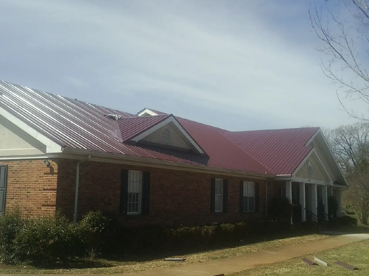 Red metal roof with gabled entries on a long brick building, from a Hail Damage Roof Repair job in Molino