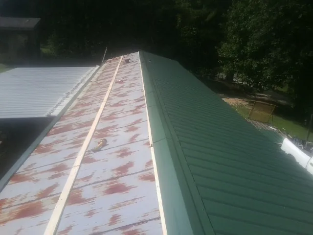 Old rusted panels beside newly installed green metal roofing — Wind Damage Roof Repair by Roofing Brothers in Molino