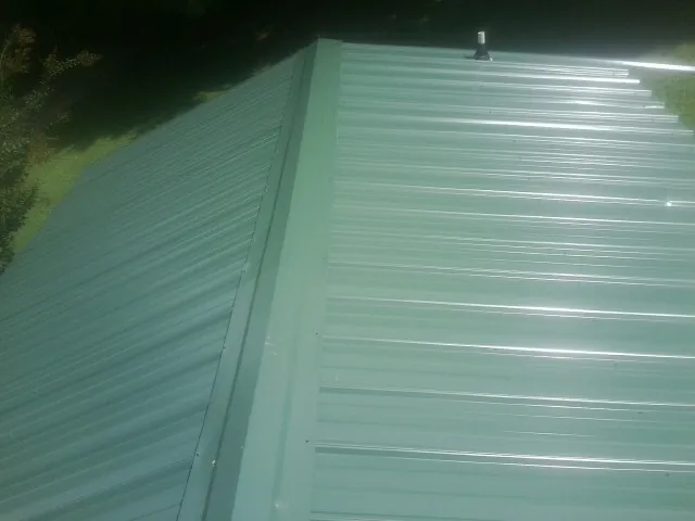 New green metal panels meeting at the ridge of a roof — Flat Roof Repair work by our crew in Molino
