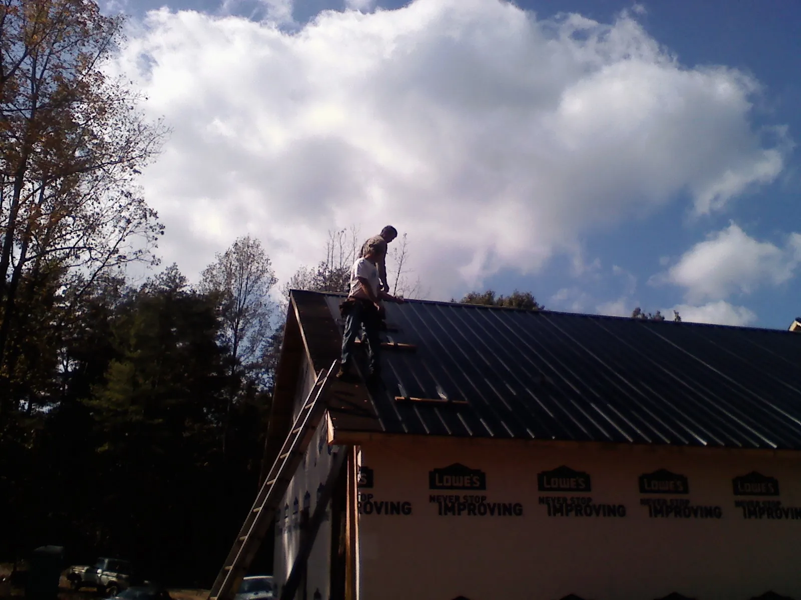 Roofer fastening dark metal panels high against a cloudy sky, from a Roof Inspection job in Molino
