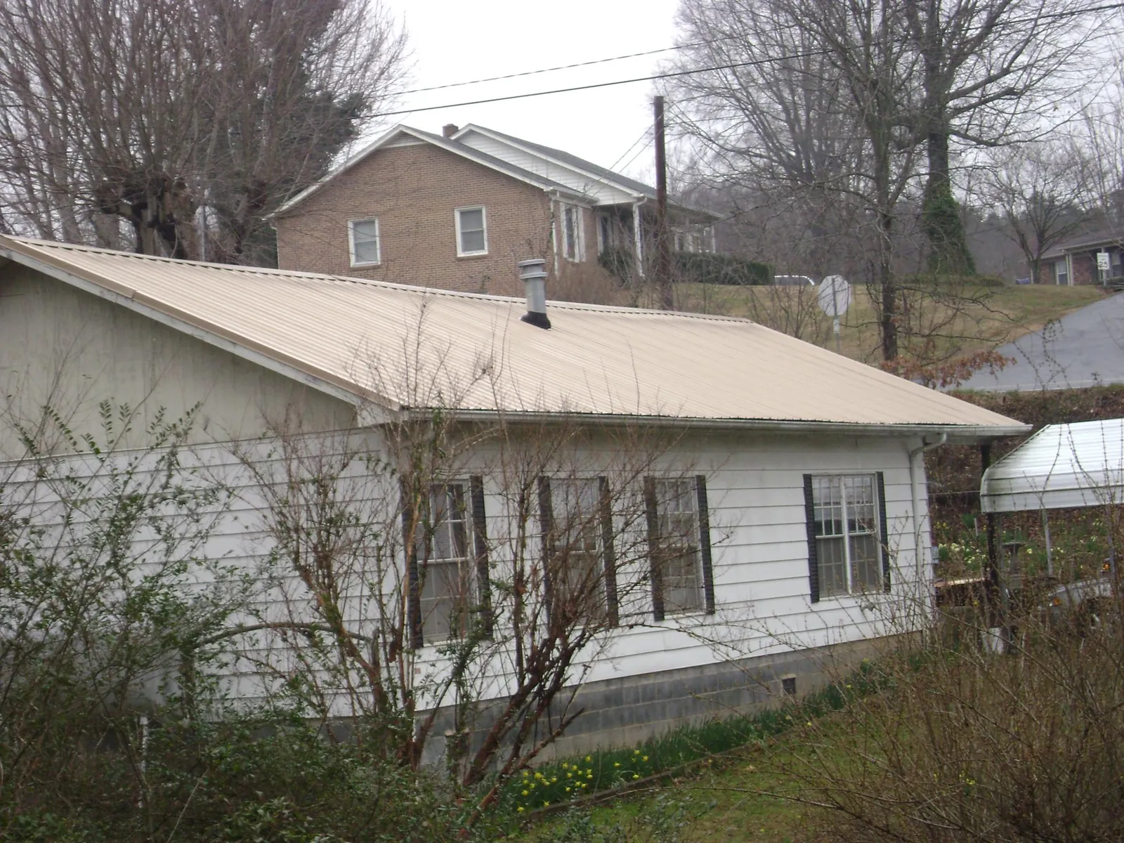 Tan metal roof on a white sided house set into a hillside — Commercial Roofing by Roofing Brothers in Molino