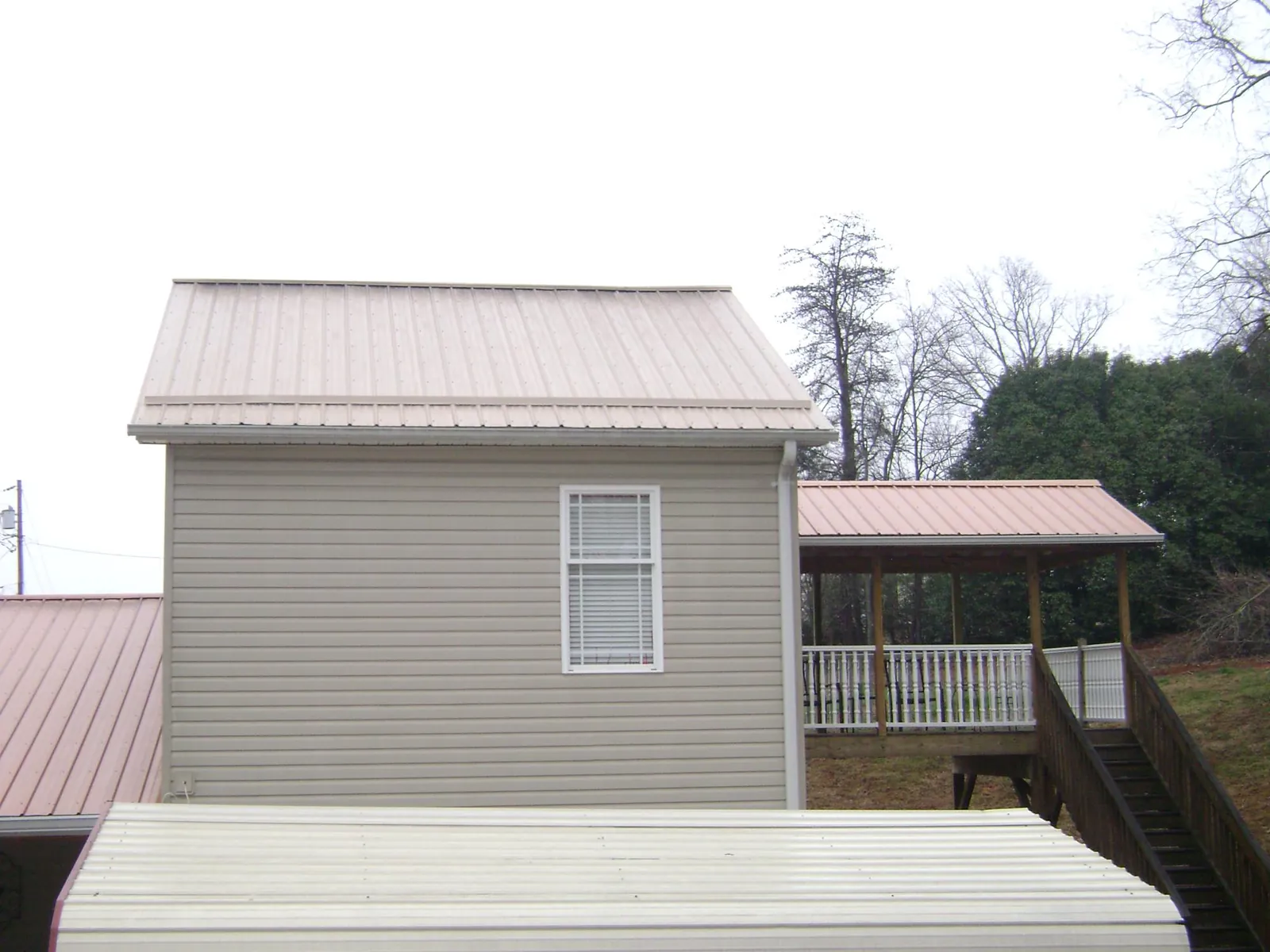 Tan metal roofs on a two story addition and attached porch, from a Roof Replacement job in Molino